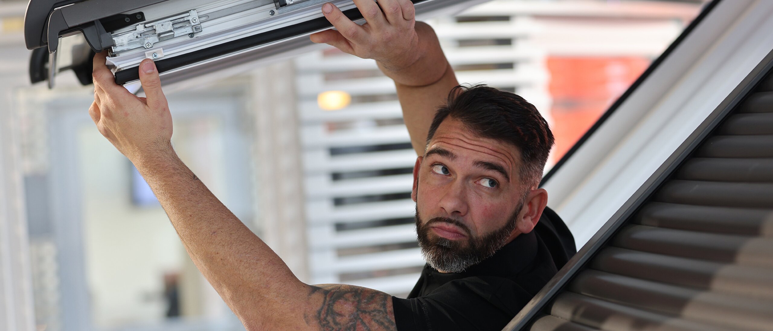 Ein Mann der aus einem offenen Dachfenster herausragt und den Fensterflügel des offenen Dachfensters nach oben drückt. 